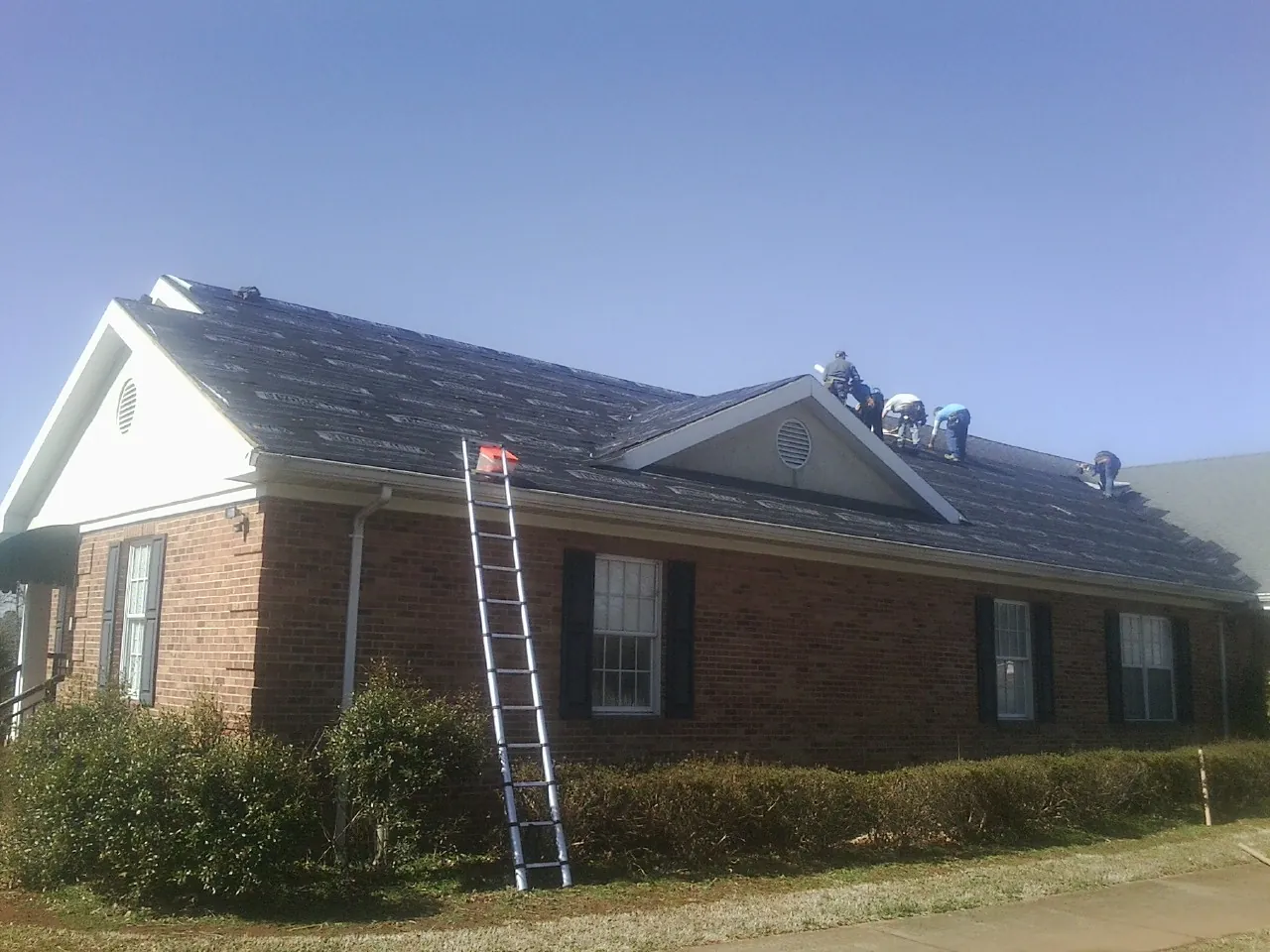 Crew tearing shingles off a brick ranch roof with a ladder set — Emergency Roof Repair work by our crew in Davenport