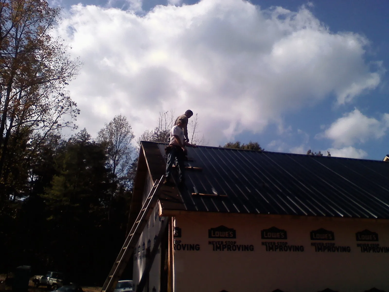 Roofer fastening dark metal panels high against a cloudy sky, from a Roof Inspection job in Davenport
